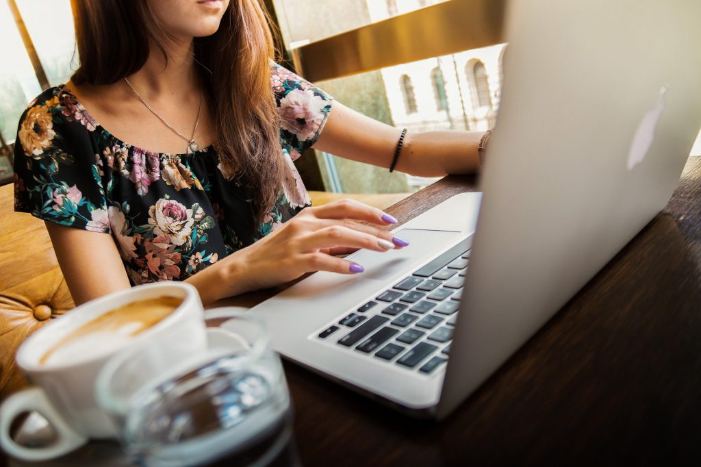 Woman sitting at laptop with a cappuccino.